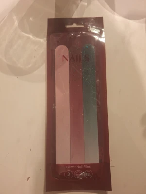 Glittriga nagelfilar 3-pack - Tre glittriga nagelfilar i olika färger: ljusrosa, röd och grön. Filarnas längd är 18 cm och de har medium grit (180/180). Perfekt för att fixa snygga naglar hemma med lite extra sparkle. Kommer i en snygg förpackning.
