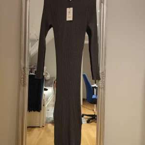 Mörkgrå ribbad långklänning Object - Snygg mörkgrå långklänning från Object med ribbad struktur och lång ärm. Klänningen har en tight passform och rund halsringning. Perfekt för dig som gillar en stilren och enkel look med lite edge.