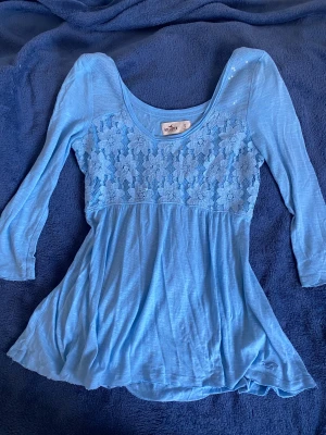 vintage blommig babydoll top Hollister - Supersöt ljusblå blus från Hollister med blommig spets över bröstet och paljettdetaljer på axeln. ✨✨✨ Modellen har trekvartsärm och en flowy, lätt utsvängd nederdel. Toppen är rare och vintage från 2000-talet!!🤩🤩 En liten fläck i ryggen som syns på sista bilden. S men passar xs-s