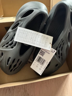 Adidas Yeezy Foam Runner svart strl 39 - Säljer ett par oanvända Adidas Yeezy Foam Runner i svart. De har en futuristisk design med många hål och rundade former, tillverkade i lätt syntetmaterial. Perfekt för dig som gillar streetwear och vill sticka ut med något unikt på fötterna.  Snyggt utseende designat av Kanye West.