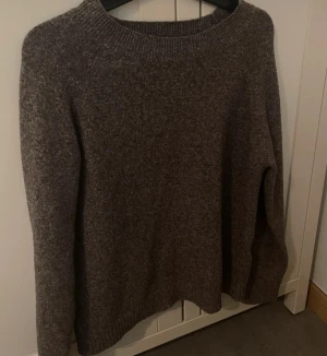 Brun stickad tröja med rund hals - Mysig grå/brun stickad tröja med rundad hals och långa ärmar. Perfekt för kyliga dagar och enkel att matcha med jeans eller kjol. Ribbstickade muddar vid hals, ärmslut och nederkant ger en snygg och klassisk look.