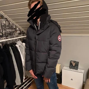 Canada Goose jacka - Säljer en svart dunjacka från Canada Goose med huva och klassisk logga på ärmen. Jackan har dragkedja och knappar framtill, quiltad design och är långärmad. Perfekt för kalla dagar och har en clean, stilren look som funkar till jeans och hoodie. Den är S passar M                                                             obs bara testad inte använd nånting