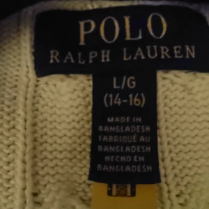 Vit kabelstickad tröja Polo Ralph Lauren - Vit kabelstickad tröja från Polo Ralph Lauren med klassisk rund hals och broderad logga på bröstet. Tröjan har ribbade muddar vid ärmslut och nederkant, och är tillverkad i mjuk bomull. Tröjan är i absolut nyskick och kommer från ett djur och rökfritt hem. Strl.170