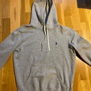 Grå hoodie från Polo Ralph Lauren - Snygg grå hoodie från Polo Ralph Lauren i storlek XS. Tröjan har huva med snörning, magficka och ett litet broderat logomärke på bröstet. Perfekt för chill dagar och enkel att matcha med jeans eller joggers. Allt är i bra skick förutom en fläck på en av snöret. Undrar ni något är det bara att skriva!