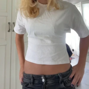 Vit croppad topp med knyt i sidan - Säljer en vit croppad topp med korta ärmar och snygg knytning i sidan. T-shirten har en enkel och clean look med rund hals och är tillverkad i mjukt bomullstyg. Perfekt för dig som gillar en fräsch och trendig stil.