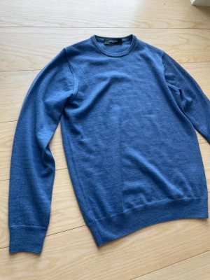 Blå merino ull tröja från Lawrence Grey - Snygg blå stickad tröja från Lawrence Grey med rund hals och långa ärmar. Enkel och stilren design utan mönster, perfekt att matcha med jeans eller chinos. Mjuk och skön kvalitet som sitter bra på kroppen.