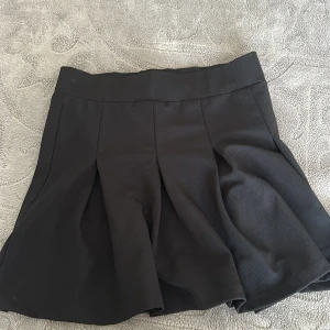 Svart plisserad kortkjol från 157 - Svart kortkjol från 157 i storlek XS. Kjolen har bred linning och snygga plisserade veck som ger en klassisk och trendig look. Perfekt att styla med en oversized hoodie eller en tight topp för en cool vibe.