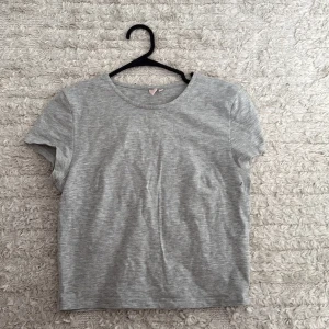 Grå t-shirt från Nelly, storlek S - En enkel och stilren grå t-shirt från Nelly i storlek S. T-shirten har rund hals och korta ärmar, tillverkad i mjuk bomull som känns skön mot huden. Perfekt för dig som gillar minimalistisk och clean look.