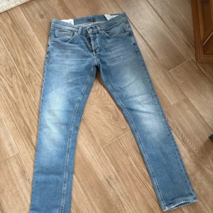 Dondup George skinny fit strl 32 - Snygga ljusblå jeans från Dondup i klassisk femficksmodell med orangea sömmar och Dondup märke på bakfickan. Jeansen har rak passform och är tillverkade i mjukt denimtyg som ger en skön känsla. Perfekt för dig som gillar stilrena och tidlösa jeans.
