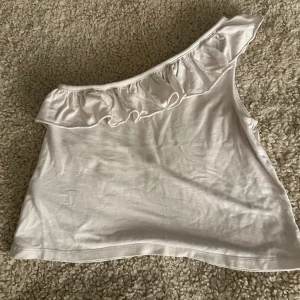 Vit oneshoulder topp med volang Gina Tricot - Säljer denna jätte söta topp då den inte används eftersom den är för liten. Jätte fint skick och jätte skön 💕 Pris kan diskuteras