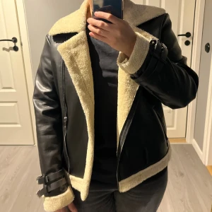 Svart teddyjacka med fuskpäls från DEMLI - Svart teddyjacka från DEMLI med krage och insida i beige fuskpäls. Säljer min teddy biker jacka som endast är använd några gånger .