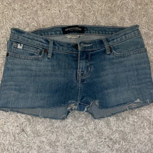 Shorts lågmidjade - Snygga blå jeansshorts från Abercrombie med stretch. Klassisk femficksdesign, lågmidjade och råa kanter med slitna detaljer. Baksidan har två fickor med dekorativ söm. Perfekta för varma dagar och chill stil.😊säljer pga att de inte passar längre, skriv gärna vid frågor!🥰