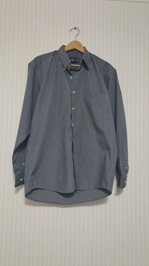 Grå skjorta från Ralph Lauren L - Snygg grå skjorta från Ralph Lauren i 100% bomull. Klassisk modell med knappar framtill, bröstficka och broderad logga i ljusgrått. Skjortan har lång ärm och en stilren, normal passform som funkar till många olika looks. Strl large. Vid frågor hör av er.