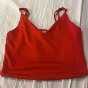 Röd linnetopp med justerbara axelband - Snygg röd linnetopp med v-ringad hals och dubbla justerbara axelband. Toppens material känns mjukt och lätt, perfekt för varma dagar. Enkel och stilren design som ger en fräsch vibe. Passar dig som gillar färg och vill ha en enkel topp med lite extra detalj på axelbanden.