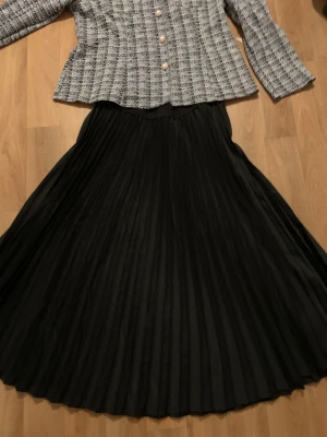 Svart plisserad långkjol - Säljer en svart plisserad långkjol med snyggt fall och klassisk look. Kjolen har hög midja och är i ett lätt, flowy material som ger en elegant siluett. Perfekt för dig som gillar stilrena och tidlösa plagg.