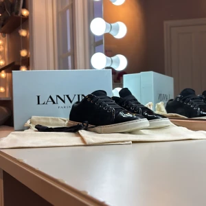 Svarta sneakers från Lanvin i mocka - Snygga svarta sneakers från Lanvin med ovandel i mjuk mocka och detaljer i blankt skinn. Skorna har rund tå, snörning och vit platt sula som ger en clean look. Perfekta för dig som gillar exklusiv stil med fräscha materialval.