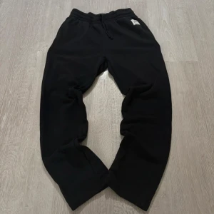 Svarta mjukisbyxor Andy by Frank Dandy - Svarta mjukisbyxor från Andy by Frank Dandy med elastisk midja och snörning. Byxorna har en relaxed passform och är tillverkade i mjukt material som är perfekt för chill dagar. Diskret logotyp-patch framtill ger en clean look.