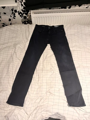 Replay Anbass mörkblå jeans W30 L32 - Snygga Replay Anbass jeans i mörkblå färg med klassisk femficksdesign och raka ben. Jeansen har diskreta kontrastsömmar och Replay-logga på bakfickan. Passar dig som gillar en modern och stilren look.