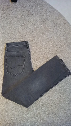 Grå jeans från Jack & Jones - Snygga grå jeans från Jack & Jones, modell Slim/Glenn. Jeansen har en smal passform med klassisk femficksdesign och svarta detaljer vid knappar och nitar. Materialet är mjukt jeans-tyg med lätt tvättad look och raka ben. Köpta för 1100 i butik helt nya. Pris kan diskuteras vid snabb affär 🤗🤝