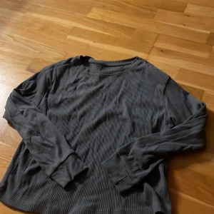 Mörkgrå ribbad långärmad tröja - Säljer en mörkgrå långärmad tröja med ribbad struktur. Tröjan har rund hals och är tillverkad i mjukt material som känns skönt mot huden. Perfekt för dig som gillar enkla och stilrena plagg med lite textur.