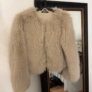 Beige pälsjacka från Gina Tricot - Säljer en fluffig och snygg beige pälsjacka från Gina Tricot i storlek XS. Jackan har långärmade ärmar, croppad passform och stängs med en diskret snörning framtill. Perfekt för dig som vill ha en trendig look med extra attityd.