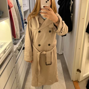 Beige trenchcoat med bälte - Säljer en snygg beige trenchcoat med dubbelknäppning och bälte i midjan❣️. Perfekt för dig som vill ha en stilren och tidlös look.😊pris kan diskuteras!!!