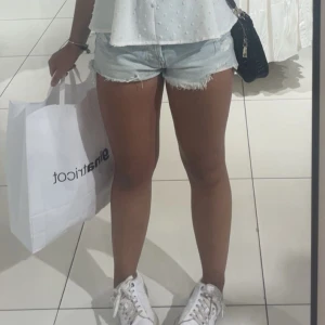 Ljusblå jeansshorts med fransad kant - Säljer ett par ljusblå jeansshorts med fransad kant och klassisk femficksdesign. Shortsen har låg midja och är gjorda i mjuk bomull, perfekta för varma dagar. Snygg och avslappnad passform som funkar till sneakers eller sandaler.