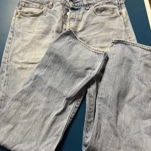 Levi's 501 ljusa jeans straight fit - Säljer ett par klassiska Levi's 501 jeans i ljusblå tvätt med raka ben och fem fickor. Jeansen har knappgylf och den ikoniska Levi's-designen med orangea sömmar. Perfekt för dig som gillar vintagekänsla och tidlös stil.