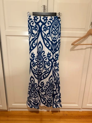 Vit och blå långkjol med mönster - Säljer en långkjol med riktigt snyggt blått och vitt mönster. Kjolen har en rak passform och resår i midjan för extra komfort. Aldrig använd