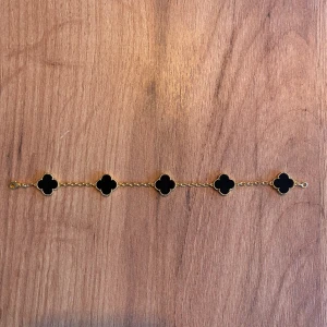 Van cleef armband - Snyggt armband med fem svarta klöverformade hängen infattade i guldfärgad kedja. Klöverhänget har en pärlad kant som ger extra lyxig känsla. Perfekt för dig som gillar stilrena och unika detaljer. Lätt att matcha med andra smycken.