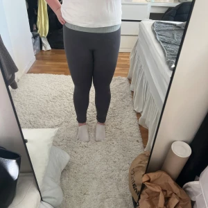 Mörkgrå leggings från Gymshark - Säljer ett par mörkgrå leggings från Gymshark med bred resår i midjan där loggan syns. De har en tight passform och är tillverkade i mjukt, stretchigt syntetmaterial som sitter skönt mot kroppen. Perfekta för träning eller när som helst!!✨💕