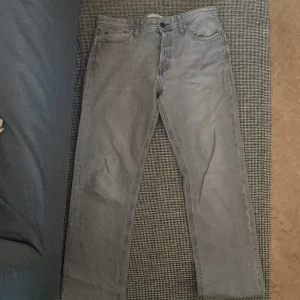 Grå jeans från Jack & Jones, 32/32 - Säljer ett par grå jeans från Jack & Jones med klassisk femficksdesign och raka ben. Jeansen har en snygg, ljusgrå tvätt och är tillverkade i slitstarkt denim. Passar dig som gillar enkel och stilren look.