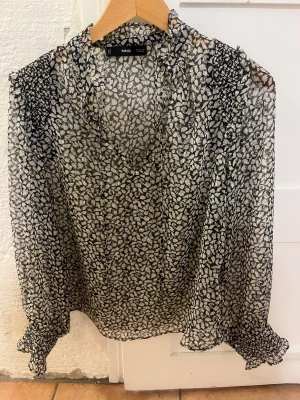 Svartvit blommig blus från Mango - Säljer en transparent svartvit blus från Mango med blommigt mönster. Blusen har långärmade ärmar med smock vid ärmslut och v-ringad hals. Materialet är lätt och luftigt! Helt oanvänd! Är storlek Xs men sitter som en S