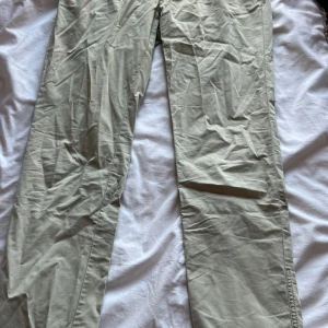 Beige chinos från J.Lindeberg slim fit - Snygga beige chinos från J.Lindeberg i slim fit-modell. Byxorna har klassisk rak passform och är tillverkade i mjuk bomull. Insidan har ett rutigt foder i rött och vitt samt detaljer med röd kant. Perfekta för en clean och stilren look.