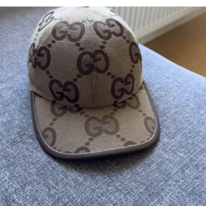 keps med GG-mönster beige/brun - Säljer en snygg keps i beige och brunt med det klassiska GG-monogrammet över hela kepsen. Justerbar rem baktill och böjd skärm. Tillverkad i slitstark bomullscanvas med exklusiv känsla. Perfekt för dig som vill sticka ut med en lyxig accessoar.