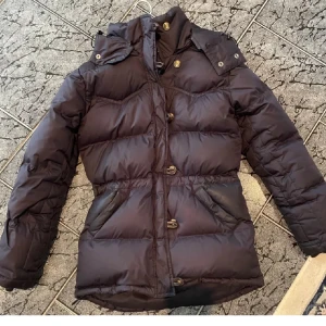 Boomerang jacka - Snygg svart vinterjacka med knappar framtill. Jackan har långa ärmar, två fickor och en hög krage som skyddar mot kylan. Perfekt för kalla dagar och enkel att matcha med olika outfits. Boomerang jacka. Nypris ca 6 000!