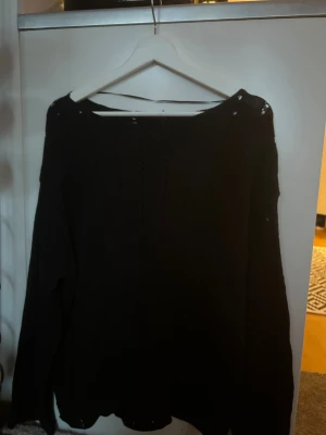 Svart stickad tröja med hålmönster - Svart stickad tröja med lång ärm och snygga vertikala hålmönster som ger en cool och lite edgy vibe. Perfekt för dig som gillar klassiska färger men vill ha något med lite extra detalj. Tröjan har en rund hals och är mjuk och skön att bära. (lite oversize)