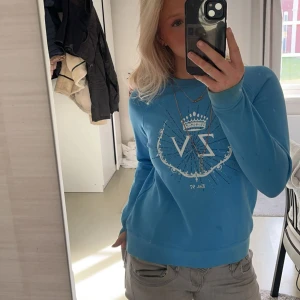 Blå sweatshirt från Zadig & Voltaire - Säljer en blå sweatshirt från Zadig & Voltaire med tryck av krona och ZV-logga framtill. Tröjan har rund hals, långa ärmar och är gjord i mjuk bomull. Perfekt för dig som gillar en chill och snygg stil.