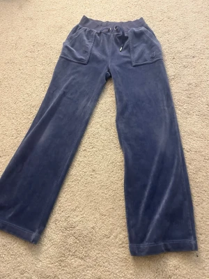 Blå velourbyxor Juicy Couture XS - Mysiga blå mjukisbyxor från Juicy Couture i velour med bred resårmidja och snörning. Byxorna har stora fickor fram och bak, samt raka ben för en chill vibe. Perfekta för dig som vill ha både stil och komfort. Är 158 cm lång och dom passar super!
