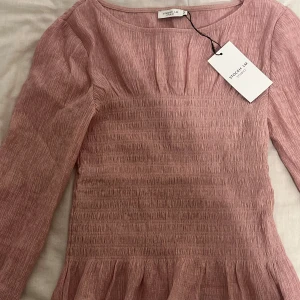 Rosa blus från Stockh LM - Supersöt ljusrosa blus från Stockh LM Studio med smockad överdel, volangkant nertill och långa ärmar med volangdetalj.💕💖💘(orginalpris:499kr)