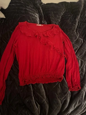 Röd volangblus från KappAhl - Säljer en röd långärmad blus från KappAhl i storlek 146-152 med volangdetaljer längs ringningen och nederkanten. Funderingar? Skriv till mig 💕