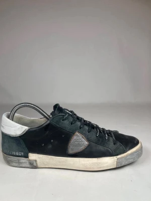 Svarta Philippe Model sneakers - Säljer ett par svarta Philippe Model sneakers med vit häl och grå detalj på sidan. Skorna har snörning med logotyp på skosnörena och slitna detaljer på sulan. Materialmix av skinn och mocka ger en schysst kontrast och streetkänsla.