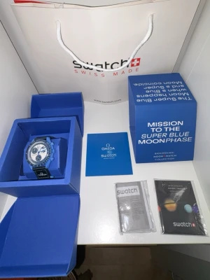 Blå Omega x Swatch MoonSwatch väst - Snygg klocka i blått från Omega x Swatch MoonSwatch-kollektionen. Klockan har en sportig look med tydliga detaljer och logga framtill. Tillverkad i biokeramiskt material som känns modernt och lätt. Perfekt för dig som vill sticka ut med en unik accessoar.