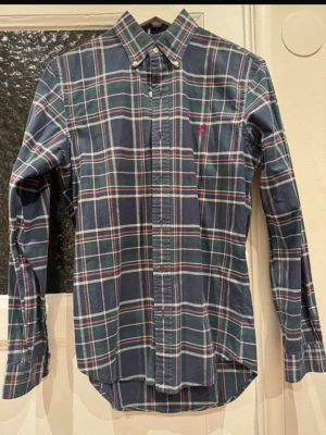 Rutig skjorta Polo Ralph Lauren S - Klassisk rutig skjorta från Polo Ralph Lauren i slim fit. Skjortan har blå, gröna och röda toner med knappar hela vägen och ikonisk broderad logga på bröstet. Tillverkad i mjuk bomull med lite stretch för extra komfort.
