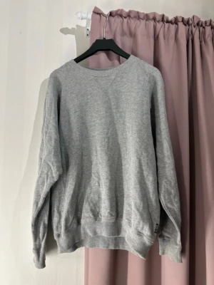 Grå sweatshirt från Clique, storlek S - En basic grå sweatshirt från Clique i storlek S. Tröjan har rund halsringning, ribbade muddar vid ärmslut och nederkant samt en relaxed passform. Perfekt till chill dagar och enkel att matcha med allt. Materialet är mjukt och skönt