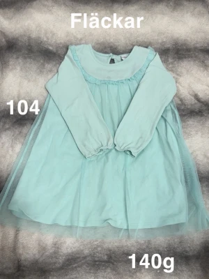 Ljusblå långärmad klänning med tyll - Söt ljusblå klänning med långa ärmar och ett lager av tunn tyll över kjolen. Rund halsringning och diskret volangdetalj framtill. Perfekt för dig som gillar en drömmig och lekfull stil.🌸Fläckar. Storlek 104 