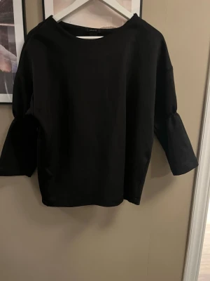 Svart blus med vida ärmar från Lindex - Säljer en svart blus från Lindex med rund halsringning och vida trekvartsärmar.