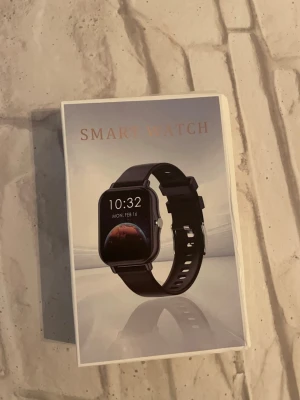 Smart Watch - Ny smartklocka i originalförpackning. Inkluderar svart silikonarmband, extra metallarmband och laddare. Klockan har fyrkantig display och flera smarta funktioner. Perfekt för dig som vill hålla koll på hälsa och notiser. Produkten ser oanvänd ut och levereras komplett.