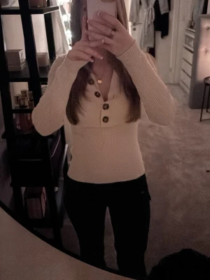 Beige ribbad tröja från KappAhl - Säljer en beige ribbad tröja från KappAhl i storlek XS. Tröjan har lång ärm, v-ringning och fyra stora, mönstrade knappar framtill. Materialet är stretchigt och mjukt, perfekt för lager på lager under höst och vår.