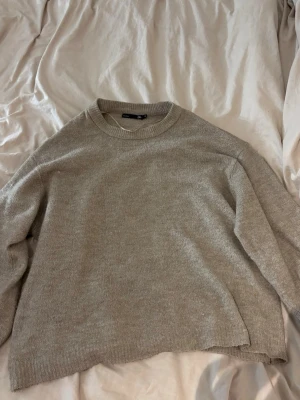 Beige stickad tröja  - Mysig beige stickad tröja  med rund halsringning och långa ärmar. Tröjan har en avslappnad passform och ribbade muddar vid ärmslut och nederkant. Perfekt för lager på lager under kyliga dagar.